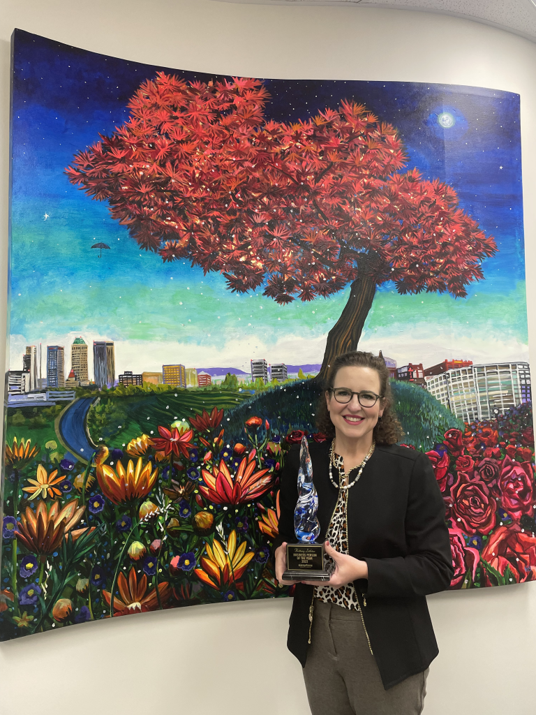 Littletonlegal Brittany Littleton holding her BA Chamber award in front of Tulsa to BA painting